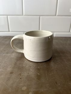 a white coffee cup sitting on top of a wooden table next to a tiled wall