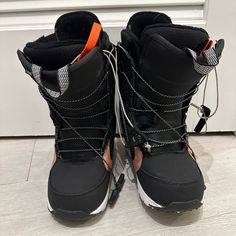 a pair of black snow boots with orange and white laces sitting on the floor