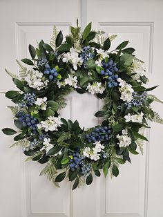 a wreath with white and blue flowers on it hanging on the front door to welcome guests