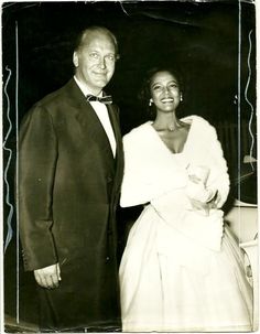 an old black and white photo of two people dressed in formal wear standing next to each other