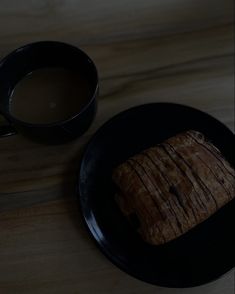 a piece of bread sitting on top of a black plate next to a cup of coffee