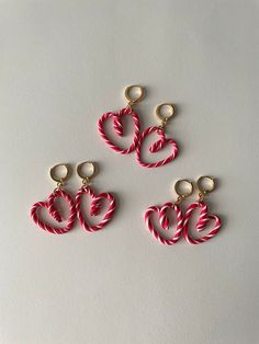 three red and white candy cane earrings on a white surface with the word love spelled in gold