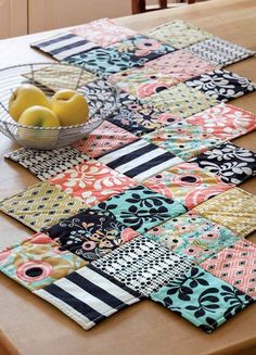 a wooden table topped with place mats covered in different types of fabrics and fruit on top of it