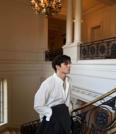 a young man in white shirt and black pants standing on stairs with chandelier