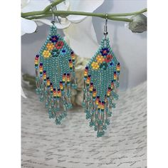 a pair of blue and yellow beaded earrings hanging from a branch with flowers in the background