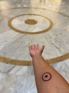 a person's arm with a small black dot tattoo on the middle of it