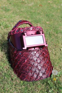 a red purse sitting on top of a lush green field