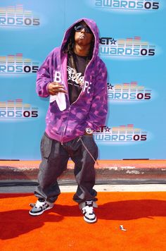 a young man in a purple hoodie and black pants standing on an orange carpet