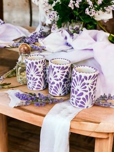 purple and white candles are sitting on a table with lavender flowers in vases next to them