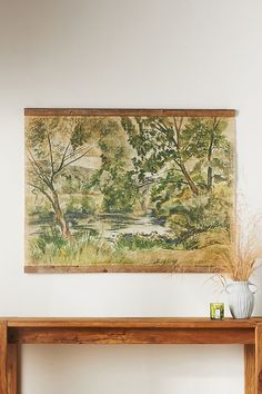 a painting hanging on the wall next to a wooden table with vases and plants