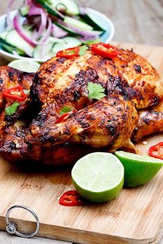 grilled chicken on a cutting board with sliced cucumber and lime wedges