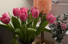 pink tulips in a vase on a table next to a window sill