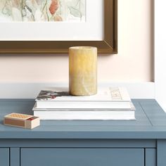 a blue table topped with books and a yellow candle next to a framed painting on the wall