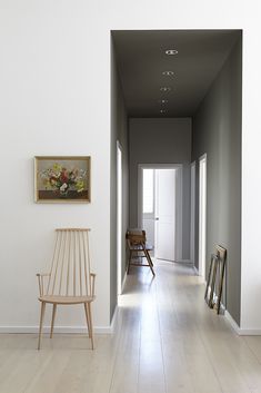 an empty hallway with a chair and pictures on the wall next to it, in front of a doorway