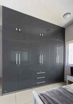 an empty bedroom with grey cabinets and white flooring on the walls, along with a large bed