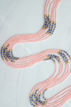 three strands of pink and blue beaded necklaces on a white tablecloth with gold accents