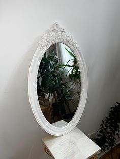 a white mirror sitting on top of a table next to a potted plant in a room