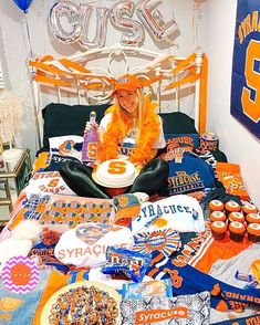 a woman sitting on top of a bed covered in orange and blue decorations with balloons