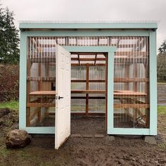 an outhouse with two doors open on dirt ground next to grass and trees in the background