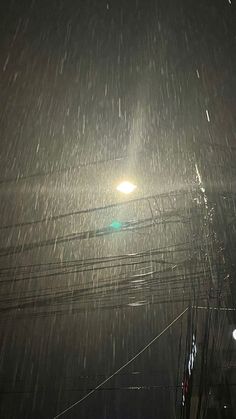 the street light is shining brightly in the dark night time sky with snow falling on it