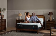 a man and woman sitting on top of a bed next to each other in a room