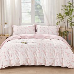 a bed with pink comforter and pillows in front of a window