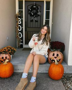 a woman sitting on the steps with two pumpkins and one is holding a cup