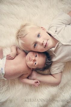 two young children laying on top of a white fluffy blanket together, one is holding the other's head