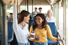 two women standing on a bus talking to each other and holding coffee cups in their hands