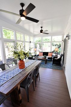 a dining room table with chairs and a ceiling fan in the middle of an enclosed patio area