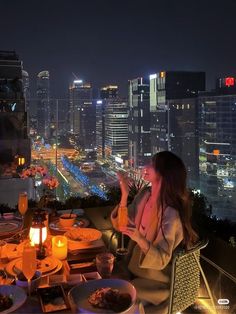 a woman sitting at a table with food and drinks in front of a cityscape