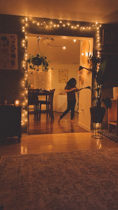 a woman is standing in the living room with her arms out and lights on behind her