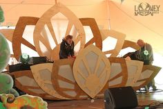 some people are standing on stage in front of a large wooden flower design and speakers