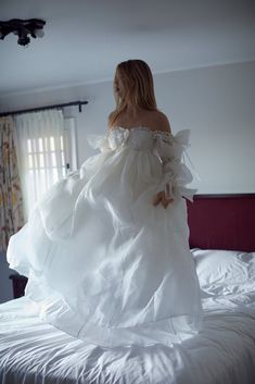 a woman in a white dress is standing on a bed