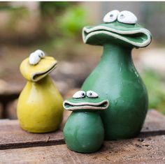 two green and yellow ceramic animals sitting on top of a wooden table in the woods