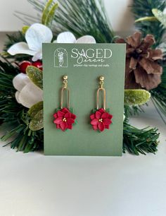 a pair of red flower earrings sitting on top of a green box next to christmas decorations