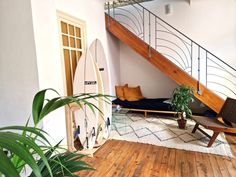 a living room with a surfboard on the floor next to a wooden stair case