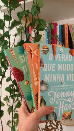 a hand holding several books in front of a plant