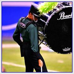 a man with a green feather on his head is holding a black marching band drum