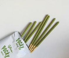 four green chopsticks in a bag on a white surface next to each other