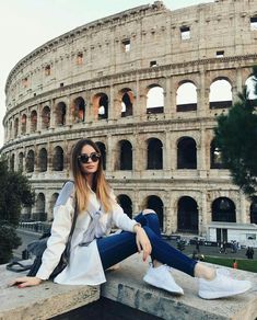 a woman sitting on top of a stone bench in front of an old building with the word colosseum