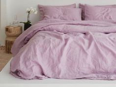 an unmade bed with pink linens and pillows in a white room next to a potted plant