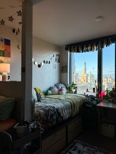 a bedroom with a bed, desk and large window looking out onto a cityscape