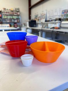 four bowls are sitting on a counter in a store, one is orange and the other is blue