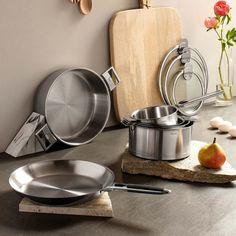 stainless steel pots and pans are on the counter next to a cutting board with an apple