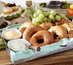 an assortment of bagels and dips on a tray with grapes in the background