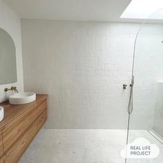 a white bathroom with two sinks and a shower in the corner, along with a large mirror on the wall