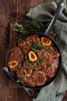 a skillet filled with meat and vegetables on top of a wooden table next to a napkin