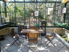 a table and chairs in a room with lots of plants inside of the glass walls