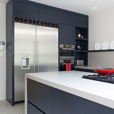 a modern kitchen with stainless steel appliances and white countertops, including a red bowl on the stove